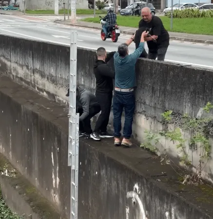 Rescued black dog resting in a man's arms on solid ground beside the canal